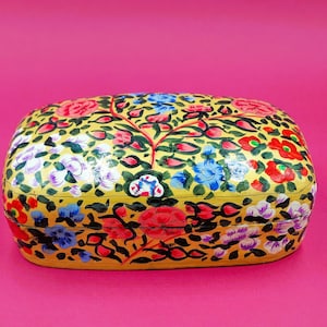 May include: A yellow rectangular box with a floral design. The box is decorated with colorful flowers and leaves. The box is made of paper mache and is a traditional Indian craft.
