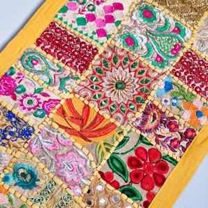 Può includere: Un runner da tavolo patchwork colorato con un bordo giallo. Il runner è realizzato con diversi tessuti con motivi floreali ricamati e dettagli a specchio.