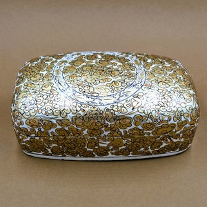 May include: A white rectangular box with a gold and orange floral design. The box is made of paper mache and has a hinged lid.