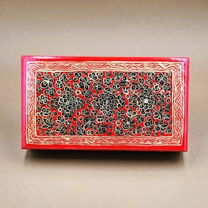 May include: A red wooden box with a black and gold floral design. The box is closed and has a hinged lid.