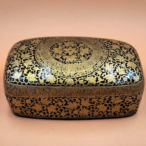 May include: A black rectangular box with intricate gold floral designs. The box is made of papier-mâché and has a hinged lid.