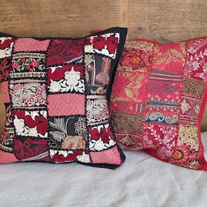 Puede incluir: Dos cojines decorativos con diseños de patchwork. Uno tiene un borde negro y una mezcla de parches rojos, rosas y negros con patrones florales y de cachemira. El otro tiene un borde rojo y un diseño de patchwork similar en tonos rojos y dorados.