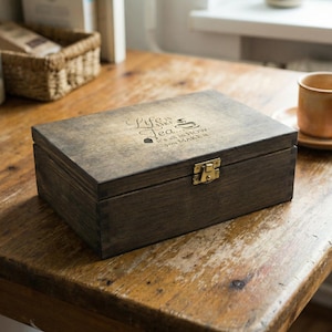 Könnte beinhalten: Eine dunkel gebeizte Teebox aus Holz mit einem Messingverschluss. Die rechteckige Box hat einen Klappdeckel. Der Deckel ist mit den Worten "Life is like tea... It's all in how you make it." graviert.