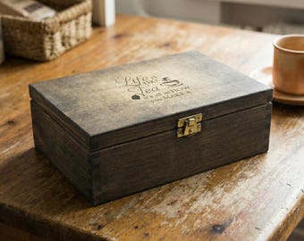May include: A dark stained wooden tea box with a brass clasp. The box is rectangular with a hinged lid. The lid is engraved with the words "Life is like tea... It's all in how you make it."
