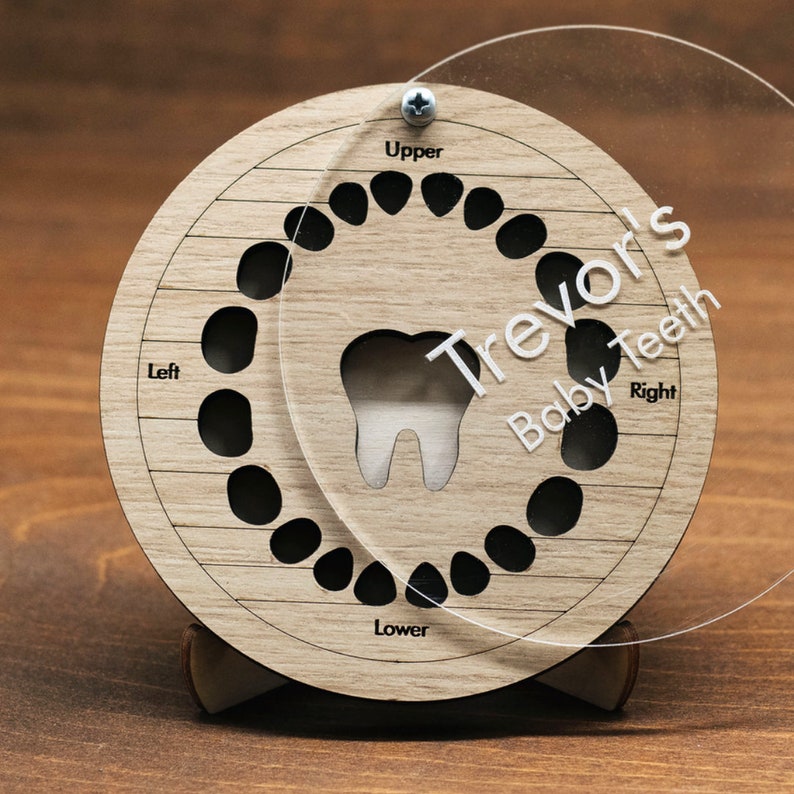 May include: A wooden baby teeth chart with a clear plastic overlay. The chart has spaces for 20 teeth, labelled "Upper", "Lower", "Left", and "Right". The overlay has the name "Trevor's Baby Teeth" printed on it.