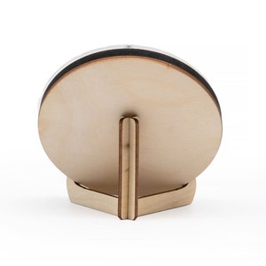 May include: A round wooden plaque with a stand. The plaque is light brown and has a smooth surface. The stand is made of the same wood and has a triangular shape.