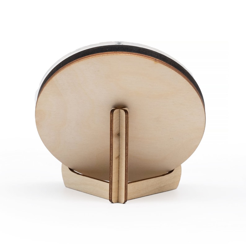 May include: A round wooden plaque with a stand. The plaque is light brown and has a smooth surface. The stand is made of the same wood and has a triangular shape.