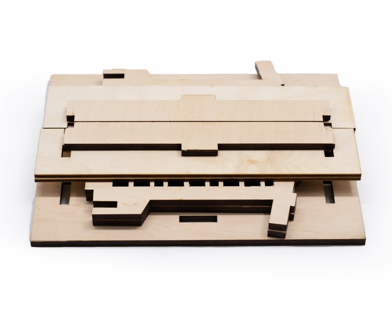 Op de afbeelding: Een ongemonteerde houten modelbouwset van een gebouw, uitgelegd in platte stukken. De stukken zijn gemaakt van lichtbruin hout en hebben ingewikkelde uitsnijdingen.