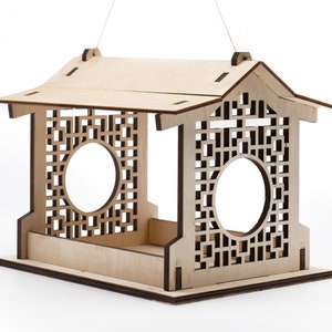 Op de afbeelding: Een houten vogelvoederhuisje met een decoratief tralieontwerp en een dak. De voederbak heeft twee ronde openingen waar vogels toegang tot het voedsel hebben.