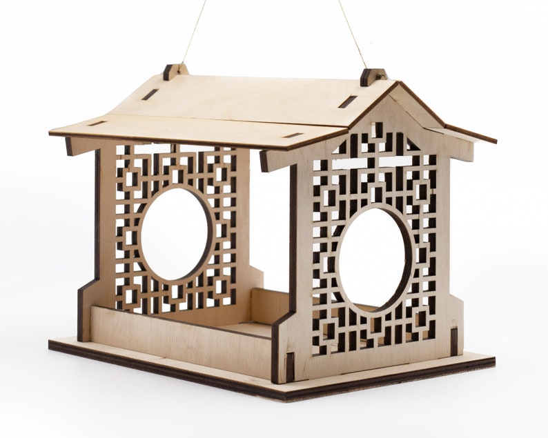 Op de afbeelding: Een houten vogelvoederhuisje met een decoratief tralieontwerp en een dak. De voederbak heeft twee ronde openingen waar vogels toegang tot het voedsel hebben.