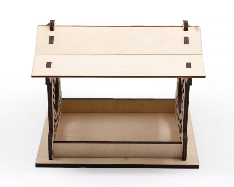 Op de afbeelding: Een houten vogelvoederhuisje met een schuin dak en een decoratief uitgesneden ontwerp. De voederbak is gemaakt van lichtbruin hout met donkerbruine accenten.