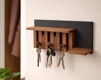 May include: A wooden key holder with a dark gray backing. The key holder has a small shelf and a series of vertical wooden slats to hold keys. Several sets of keys are hanging from the holder. The key holder is mounted on a white wall.