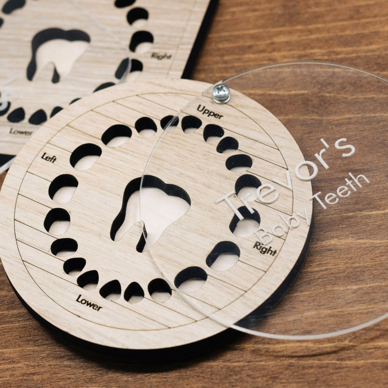 May include: A wooden baby teeth chart with a clear plastic overlay. The chart has 20 spaces for teeth, labelled "Upper", "Lower", "Left", and "Right". The overlay has the name "Trevor's Baby Teeth" printed on it.