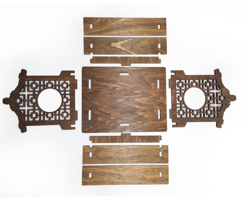 Op de afbeelding: Een houten doos met een decoratief uitgesneden ontwerp. De doos is gemaakt van donkerbruin hout en heeft een vierkante vorm. De doos is gedemonteerd en plat gelegd, waardoor de afzonderlijke onderdelen zichtbaar zijn.