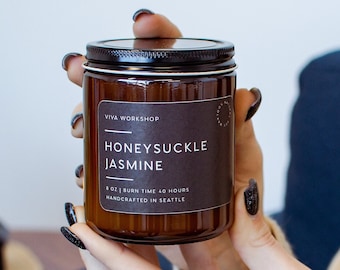 May include: A brown glass candle jar with a black label that reads "Honeysuckle Jasmine" and "8 oz | Burn Time 40 Hours | Handcrafted in Seattle".