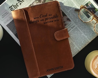 May include: A brown leather journal with the inscription "With God all things are possible Matthew 19:26" and the name "John Smith" embossed on the front cover.