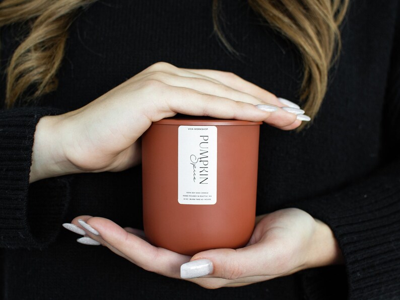 Puede incluir: Un tarro de vela de color terracota con una etiqueta blanca que dice "PUMPKIN Spice".