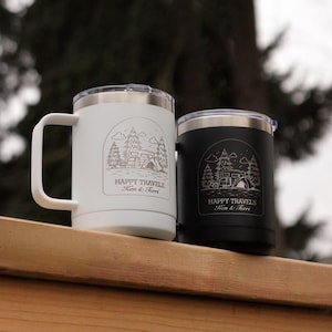 Puede incluir: Dos tazas de viaje aisladas, una blanca y otra negra, con tapas y asas plateadas. Cada taza presenta un gr&aacute;fico con tem&aacute;tica de camping con el texto "HAPPY TRAVELS Ken & Terri."