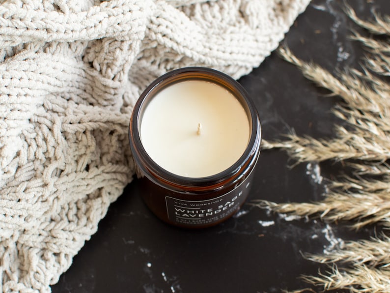 May include: A brown glass candle jar with a white soy wax candle inside. The candle has a single wick and the jar has a black label that reads "White Sage & Lavender" with the words "Viva Workshop" above the scent name.