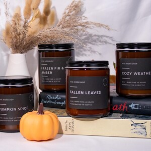 Puede incluir: Cuatro velas en frasco de vidrio &aacute;mbar con tapas y etiquetas negras. Las etiquetas dicen Viva Workshop, 9 oz, tiempo de combusti&oacute;n 40 horas, hecho a mano en Seattle, y los aromas Pumpkin Spice, Fraser Fir & Amber, Fallen Leaves, Cozy Weather.