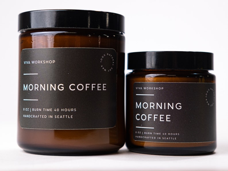 May include: Two brown glass candle jars with black labels. The larger jar is labeled "VIVA WORKSHOP MORNING COFFEE 8 OZ | BURN TIME 40 HOURS HANDCRAFTED IN SEATTLE". The smaller jar is labeled "VIVA WORKSHOP MORNING COFFEE 8 OZ | BURN TIME 40 HOURS HANDCRAFTED IN SEATTLE".