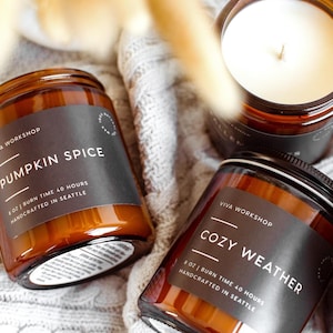 Puede incluir: Tres velas en frascos de vidrio &aacute;mbar con etiquetas negras. Una etiqueta dice PUMPKIN SPICE, 8 OZ, BURN TIME 40 HOURS, HANDCRAFTED IN SEATTLE. Otra dice COZY WEATHER, 8 OZ, BURN TIME 40 HOURS, HANDCRAFTED IN SEATTLE. Cera de color blanco.