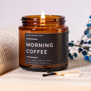 May include: A brown glass candle jar with a black label that reads "VIVA WORKSHOP" and "MORNING COFFEE". The candle is lit and the label also states "4 OZ | BURN TIME 20 HOURS | HANDCRAFTED IN SEATTLE".