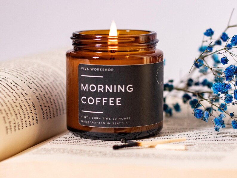 May include: A brown glass candle jar with a black label that reads "VIVA WORKSHOP" and "MORNING COFFEE". The candle is lit and the label also states "4 OZ | BURN TIME 20 HOURS | HANDCRAFTED IN SEATTLE".
