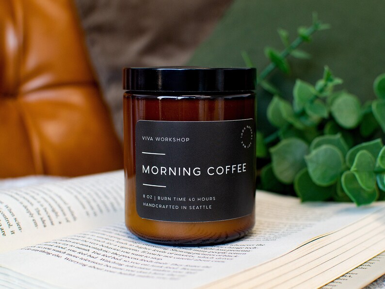 May include: A brown glass candle jar with a black lid and label. The label reads "VIVA WORKSHOP" and "MORNING COFFEE". The candle is 8 oz and has a burn time of 40 hours. It is handcrafted in Seattle.