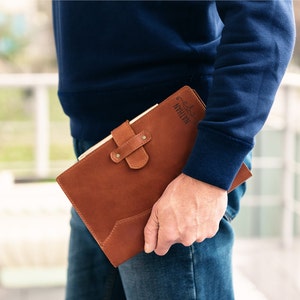 May include: A brown leather journal with a personalized inscription that reads "Nathan". The journal has a flap closure with a metal buckle and a decorative stitching detail.