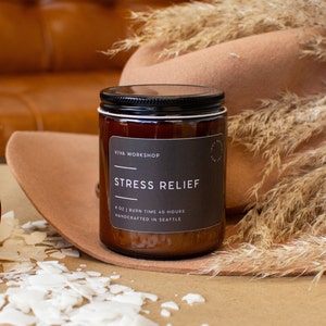 May include: A brown glass candle jar with a black label that reads "VIVA WORKSHOP" and "STRESS RELIEF". The label also states "8 OZ | BURN TIME 40 HOURS" and "HANDCRAFTED IN SEATTLE".