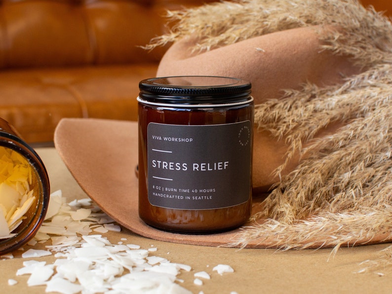May include: A brown glass candle jar with a black label that reads "VIVA WORKSHOP" and "STRESS RELIEF". The label also states "8 OZ | BURN TIME 40 HOURS" and "HANDCRAFTED IN SEATTLE".