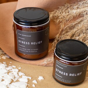 May include: Two amber glass candle jars with black lids and labels that read "Viva Workshop" and "Stress Relief". The candles are 8 oz and have a burn time of 40 hours. They are handcrafted in Seattle.