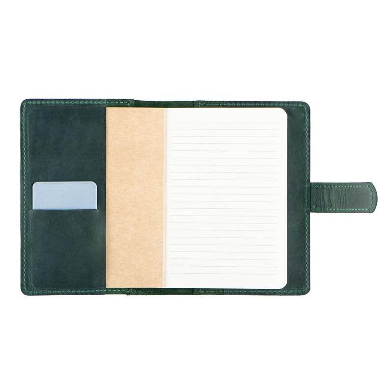 Peut inclure: Journal en cuir vert ouvert avec une carte bleu clair dans la poche. Le journal a un bloc-notes lign&eacute; et un s&eacute;parateur de couleur beige. Une sangle en cuir vert avec une fermeture &agrave; bouton-pression est sur le c&ocirc;t&eacute; droit.