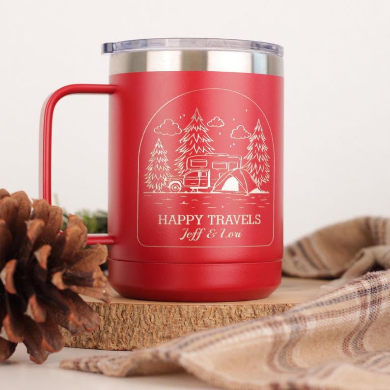 Puede incluir: Taza de viaje roja con borde y asa plateados. La taza presenta un gr&aacute;fico blanco de una caravana, una tienda de campa&ntilde;a y &aacute;rboles, con las palabras "HAPPY TRAVELS Jeff & Lou". La taza est&aacute; sobre una superficie de madera.