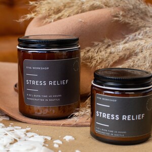 May include: Two amber glass candle jars with black lids and labels. The labels read "VIVA WORKSHOP" and "STRESS RELIEF". The candles are 8 oz and have a burn time of 40 hours. They are handcrafted in Seattle.