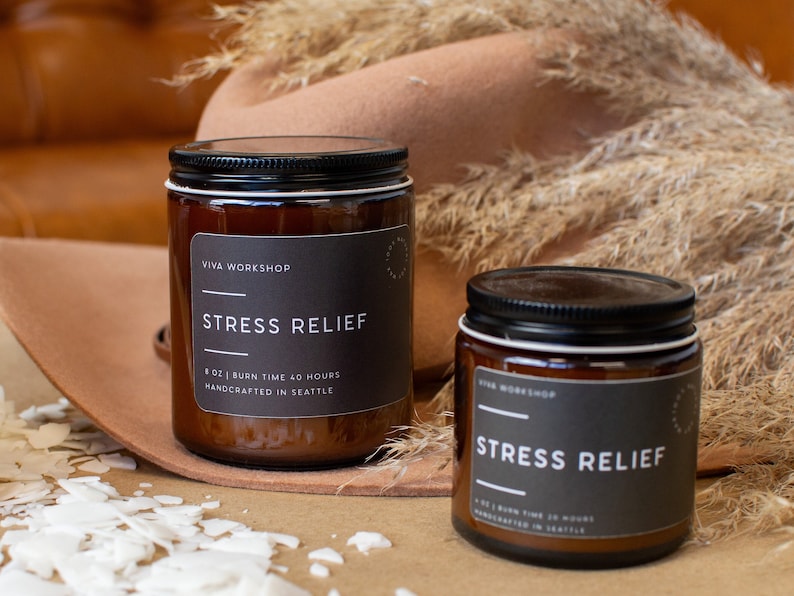 May include: Two amber glass candle jars with black lids and labels. The labels read "VIVA WORKSHOP" and "STRESS RELIEF". The candles are 8 oz and have a burn time of 40 hours. They are handcrafted in Seattle.