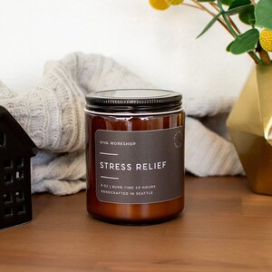 May include: A brown glass candle jar with a black lid and a white label that reads "Viva Workshop" and "Stress Relief". The label also states "8 oz | Burn Time 40 Hours | Handcrafted in Seattle".