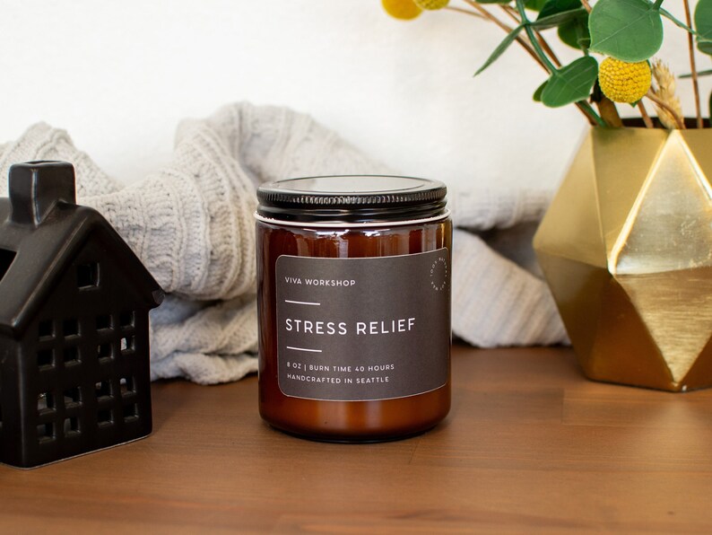 May include: A brown glass candle jar with a black lid and a white label that reads "Viva Workshop" and "Stress Relief". The label also states "8 oz | Burn Time 40 Hours | Handcrafted in Seattle".