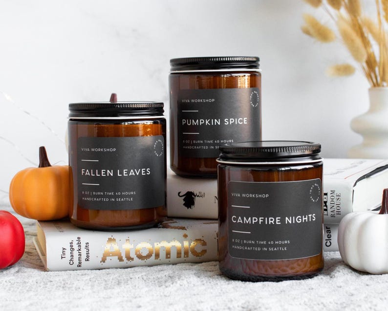 Puede incluir: Tres velas en frascos de vidrio &aacute;mbar con etiquetas negras. Las etiquetas dicen Viva Workshop, 8 oz, tiempo de combusti&oacute;n 40 horas, hecho a mano en Seattle, y los aromas Fallen Leaves, Pumpkin Spice y Campfire Nights.