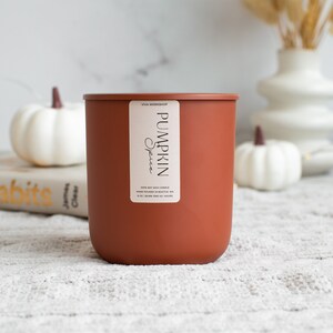 Puede incluir: Un tarro de vela de color terracota con una etiqueta blanca que dice "Viva Workshop Pumpkin Spice 100% Soy Wax Candle Hand Poured in Seattle, WA 8 oz. Burn Time 40-50 Hours"