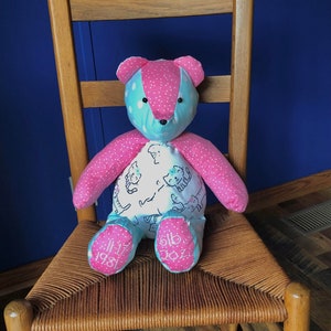 May include: A pink and blue patchwork teddy bear with a white fabric body featuring a cat print. The bear's feet are embroidered with the date "11-17-1981" and "6lb 2oz".