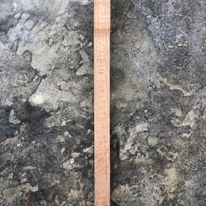 Peut inclure: Une &eacute;bauche de manche de guitare en bois brun clair, pr&ecirc;te &agrave; &ecirc;tre fa&ccedil;onn&eacute;e et finie. Le manche est lisse et pr&eacute;sente une l&eacute;g&egrave;re courbure en haut.