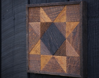 May include: A wooden wall art piece with a geometric pattern of triangles and squares in shades of brown and black. The piece is framed in a dark wood frame.