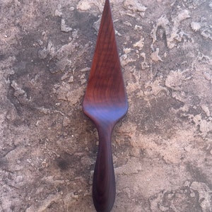 May include: A dark brown wooden cake server with a pointed tip and a long, curved handle.