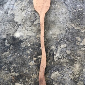 Peut inclure: Une longue cuill&egrave;re en bois avec une t&ecirc;te arrondie. La cuill&egrave;re est de couleur brun clair et pr&eacute;sente un grain de bois naturel. La cuill&egrave;re est pos&eacute;e sur une surface grise textur&eacute;e.