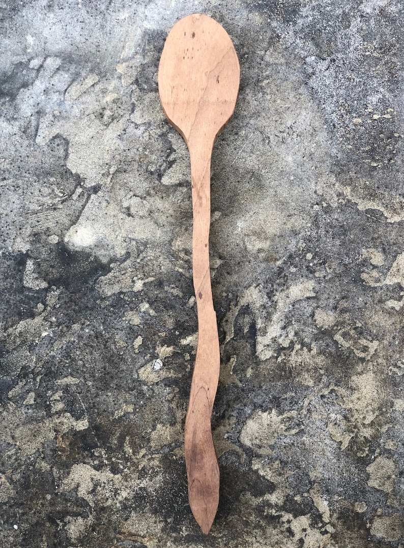 Peut inclure: Une longue cuill&egrave;re en bois avec une t&ecirc;te arrondie. La cuill&egrave;re est de couleur brun clair et pr&eacute;sente un grain de bois naturel. La cuill&egrave;re est pos&eacute;e sur une surface grise textur&eacute;e.