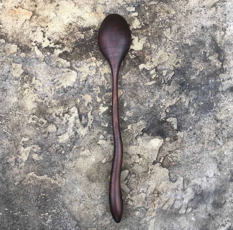 Peut inclure: Une cuill&egrave;re en bois brun fonc&eacute; avec un long manche incurv&eacute;. La cuill&egrave;re est faite d'un seul morceau de bois et a une finition lisse et polie.