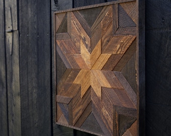 Puede incluir: Una pieza de arte de pared de madera con un diseño de estrella en forma de estallido hecha de varios tonos de madera marrón. La estrella en forma de estallido está hecha de muchas piezas pequeñas de madera que están dispuestas en un patrón geométrico.