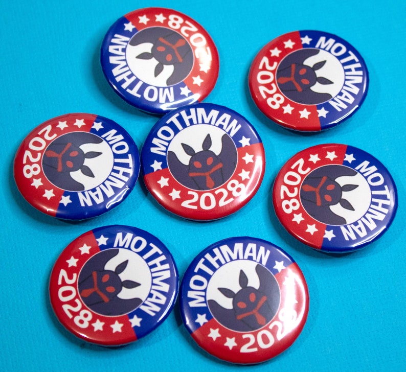 May include: Seven red, white, and blue round buttons with a black and white mothman design and the text "MOTHMAN" and "2028".